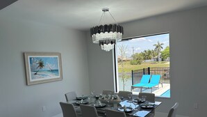 A dining area with a glass table, chairs, and a chandelier. There is a painting of a beach scene on the wall. - Gorgeous, new 3-bedroom, 3 bathroom house. heated Pool in Cape Coral , sleeps 8 (Cape Coral)