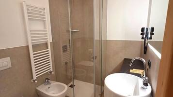 Ein modernes Badezimmer mit einer gläsernen Duschkabine, einem weißen Waschbecken und einem Bidet.