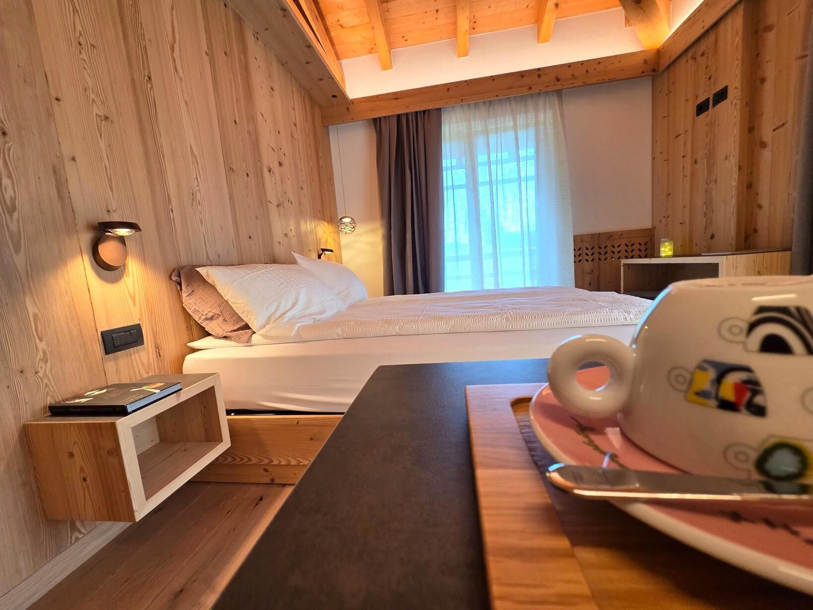 Ein gemütlicher Holzraum mit Bett, Nachttisch und einer Tasse auf Untertasse.