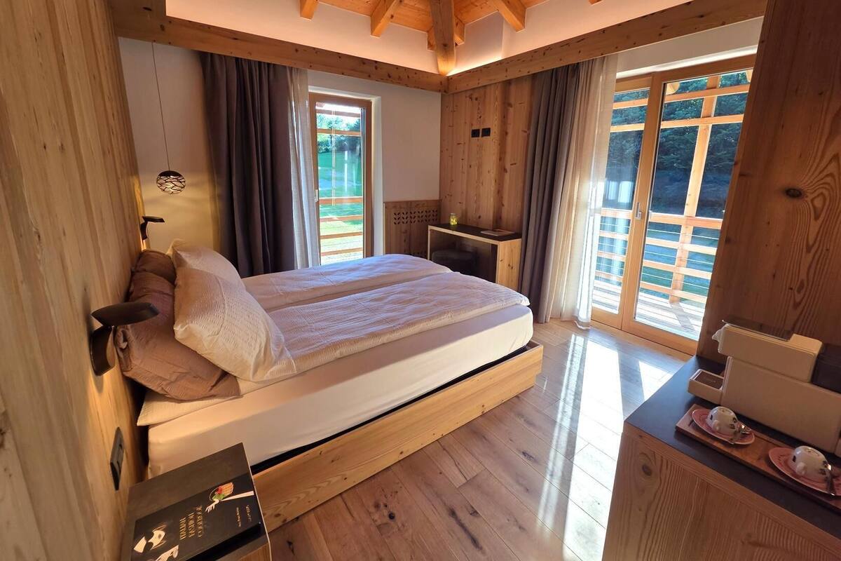 A wooden bedroom with a bed, a nightstand, a desk, and large windows.