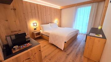 Una habitación con paneles de madera, una cama, mesitas de noche, un escritorio con una computadora y un ventanal con cortinas.
