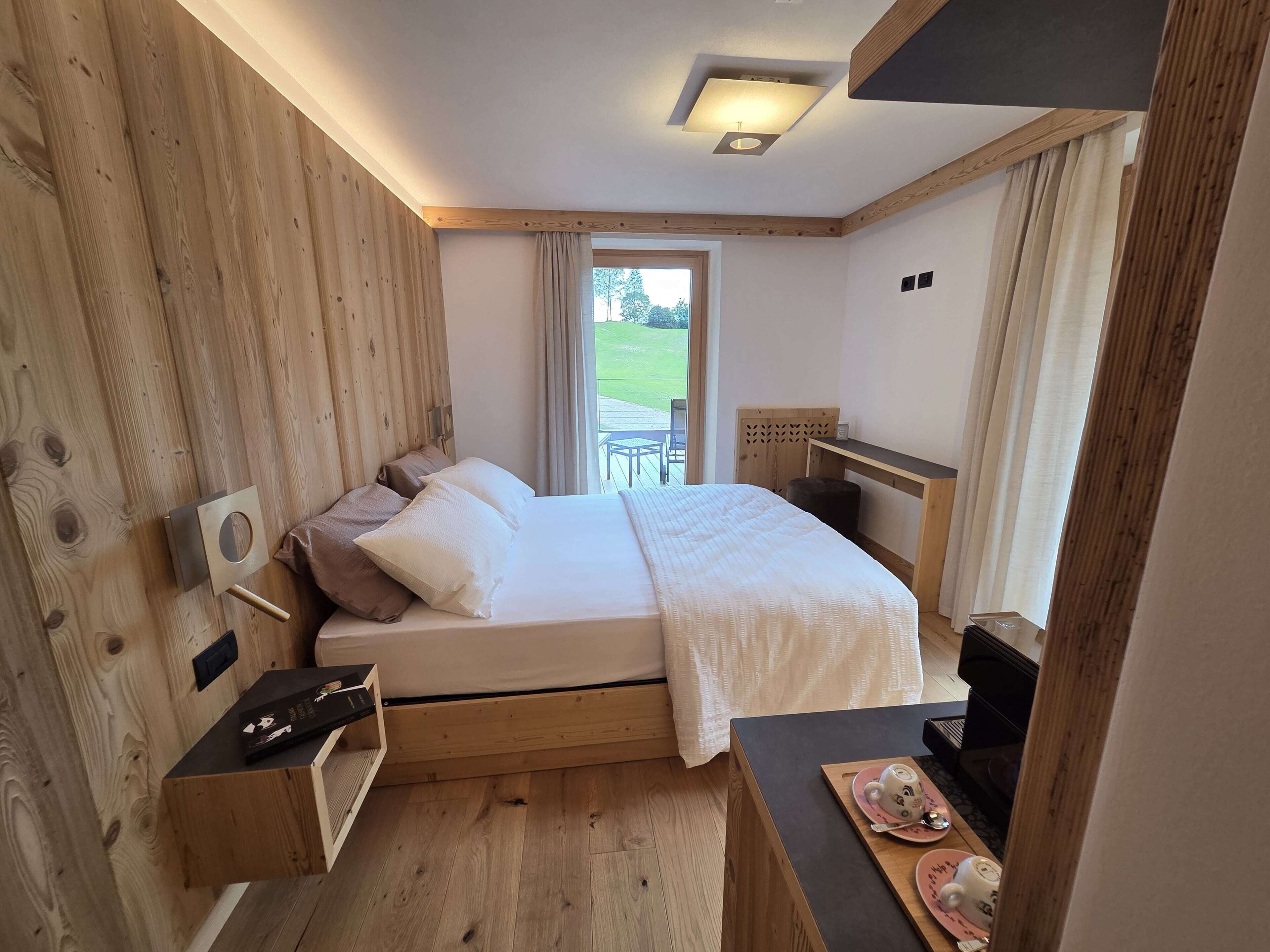 Ein Schlafzimmer mit einem hölzernen Bett, einem Nachttisch, einem Schreibtisch und einem Fenster mit Blick ins Freie.