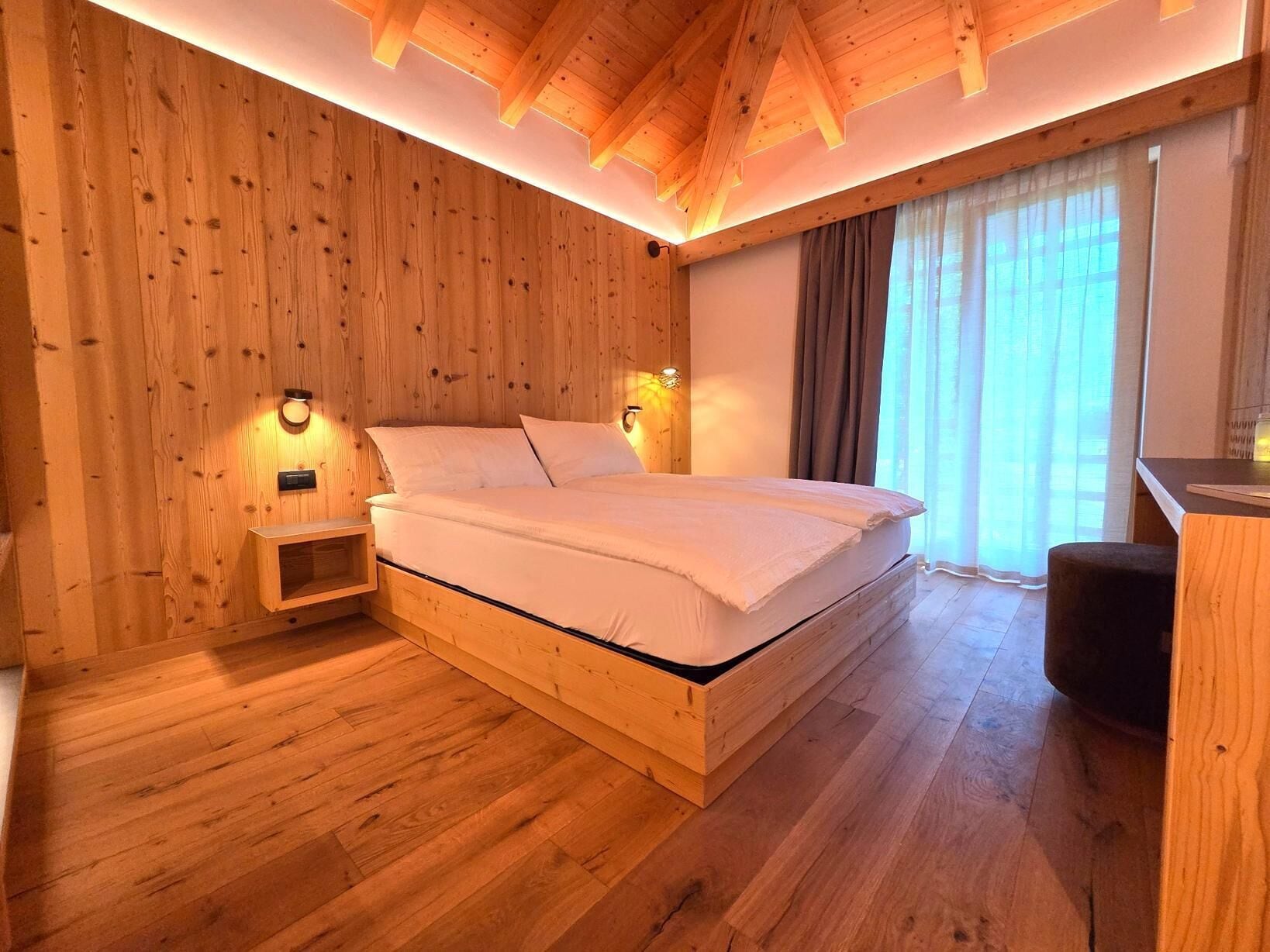 Ein Schlafzimmer mit Holzwänden, einem Bett, Nachttischlampen und einem Fenster mit Vorhängen.