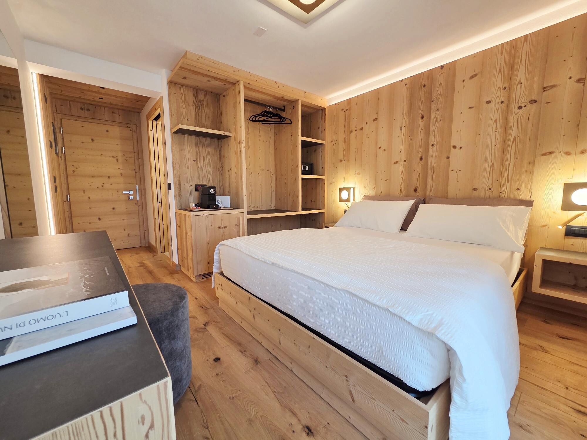Una habitación con paneles de madera, una cama, un escritorio pequeño y una mesita de noche.