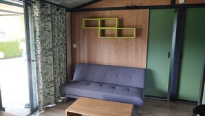 A modern living room with a grey sofa, a wooden coffee table, and a green wall with a geometric shelf. - Superb Portland Chalet, 3 bedrooms, sleeps up to 7, all comforts (Évron)