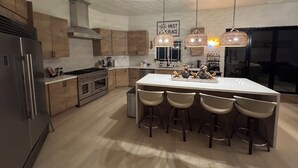 A modern kitchen with wooden cabinets, stainless steel appliances, and a central island with bar stools. - Welcome to San Diego’s Poway Paradise, your private oasis on Sycamore Canyon! (Poway)