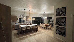 A modern kitchen with a central island, pendant lighting, and a dining area with a wooden table and chairs. - Welcome to San Diego’s Poway Paradise, your private oasis on Sycamore Canyon! (Poway)