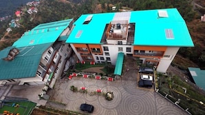 A multi-story building with a green roof, a parking area with a circular driveway, and a small garden with circular patterns.
