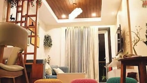 A cozy living room with a wooden ceiling, a sofa, a chair, and three colorful knitted poufs.