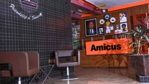Un espace d’accueil avec un mur carrelé, un comptoir de réception, une chaise et une enseigne portant l’inscription « Amicus ».