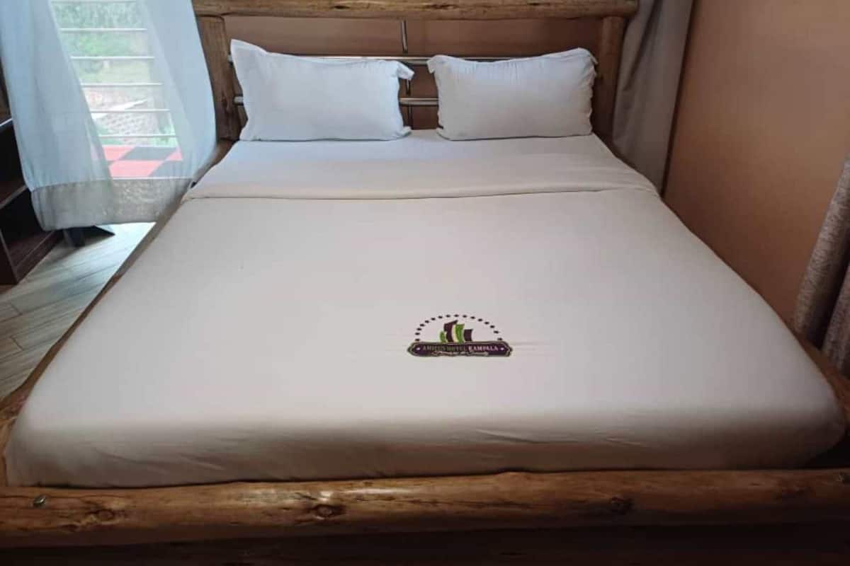 A single bed with a wooden headboard, white bedding, and a logo on the bedspread.