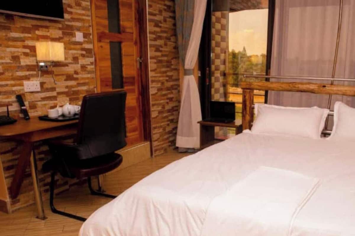 A hotel room with a large bed, a desk with a chair, a television, and a window with curtains.