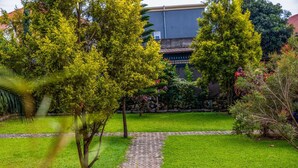 Un jardin avec un chemin pavé, une végétation luxuriante et un bâtiment en arrière-plan.