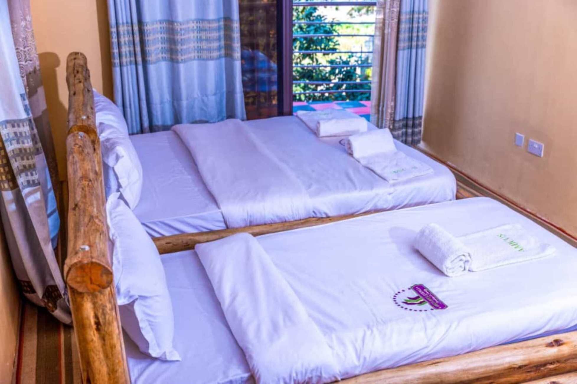 Habitación con dos camas, cada una con ropa blanca de cama y almohadas, cabeceros de madera y una ventana con cortinas.