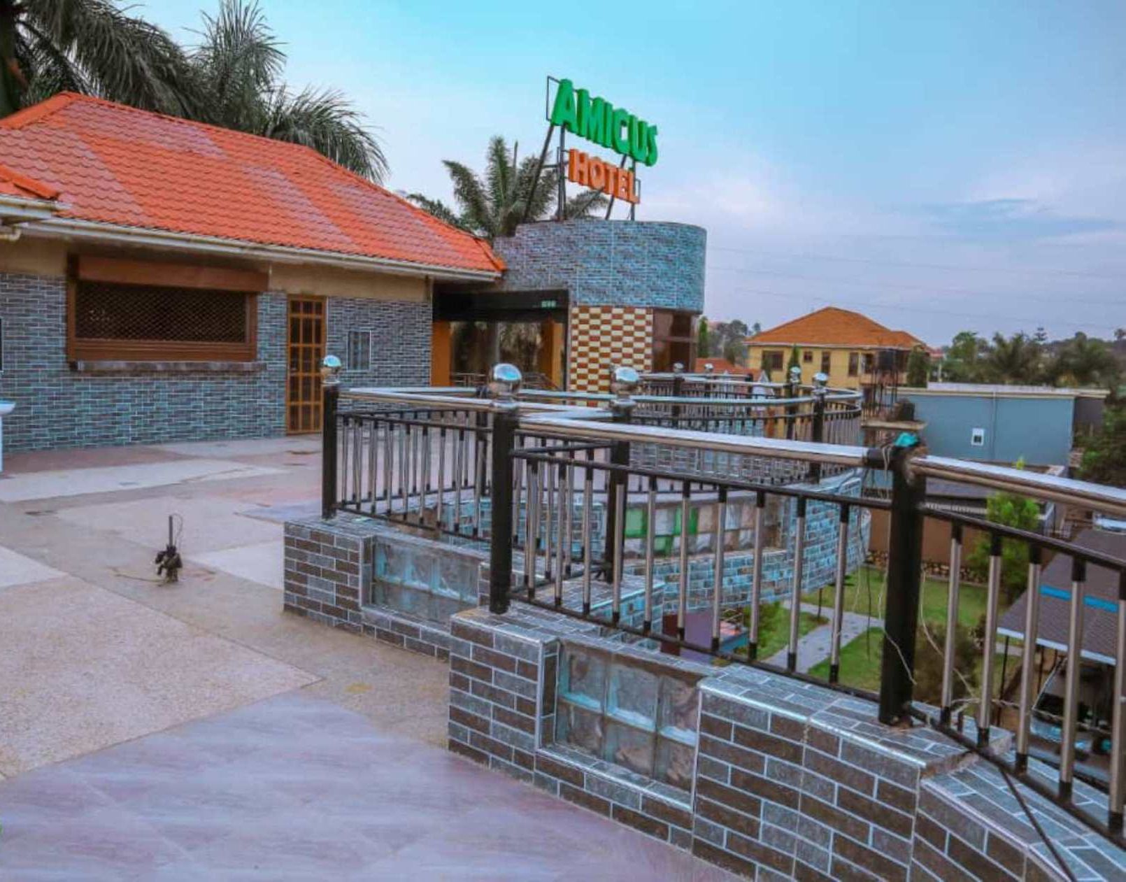 A hotel with a tiled roof, a signboard, and a paved area with a railing.