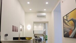 A modern kitchen with white cabinets, a dining area with a table and chairs, and a hallway with a curved counter and a painting on the wall. - Elysium Relais (Naples)