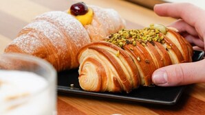 A croissant with a cherry and a sprinkle of nuts on a black plate. - Elysium Relais (Naples)