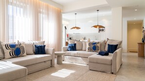 En moderne stue med et beige sofasæt, et lille rundt sofabord og et stort vindue med lette gardiner.