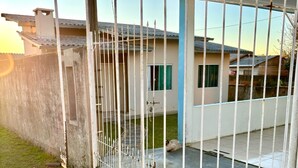 A gated entrance to a residential property with a concrete driveway and a blue and white house in the background. - Cozy house in Lages, 5 minutes from the pine nut festival. (Lages)