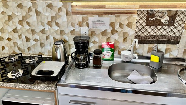 A kitchen with a gas stove, coffee maker, and a sink. There is a patterned backsplash and a shelf above the sink. - Cozy house in Lages, 5 minutes from the pine nut festival. (Lages)