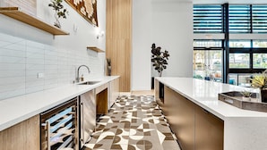 A modern kitchen with a geometric patterned floor, wooden shelves, and a view through large windows.