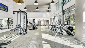 A modern gym with exercise equipment, large windows, and a brick floor.