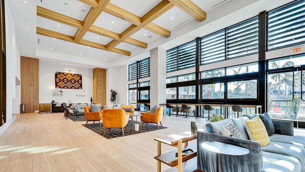 A spacious lobby with a wooden floor, a grey sofa, orange chairs, and large windows with blinds. - nr Downtown San Diego & Shops | Pet-friendly 1BR in Mission valley (San Diego)