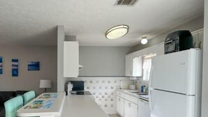 A compact kitchen with a central island, white cabinets, and a refrigerator. - The Sandy Nest • 3BR Coastal Comfort in PCB (Panama City Beach)