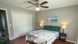 A bedroom with a bed, two bedside lamps, a ceiling fan, and a door. - The Sandy Nest • 3BR Coastal Comfort in PCB (Panama City Beach)
