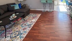 A spacious living room with hardwood flooring, a ceiling fan, a sofa with cushions, a coffee table, and a colorful rug. - The Sandy Nest • 3BR Coastal Comfort in PCB (Panama City Beach)