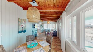 A spacious living area with a high ceiling, wooden beams, and large windows offering a view of the outside. - Charming 3br/2ba Boho Beach Cottage in Gulf Shores (Gulf Shores)