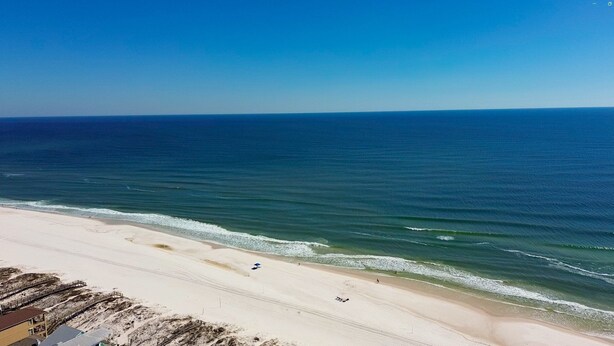 A beach with a clear view of the ocean, a sandy shoreline, and a few people walking along the beach. - Charming 3br/2ba Boho Beach Cottage in Gulf Shores (Gulf Shores)