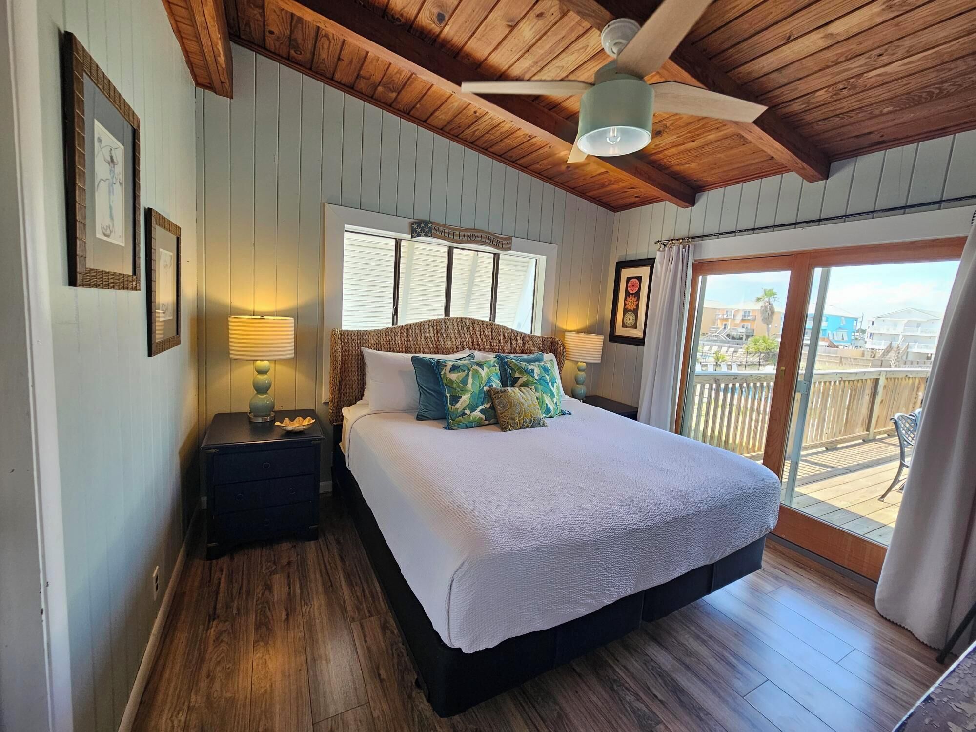 Una camera da letto con soffitto in legno, un letto con molti cuscini, un comodino con una lampada e vista sull'esterno tramite una porta scorrevole.