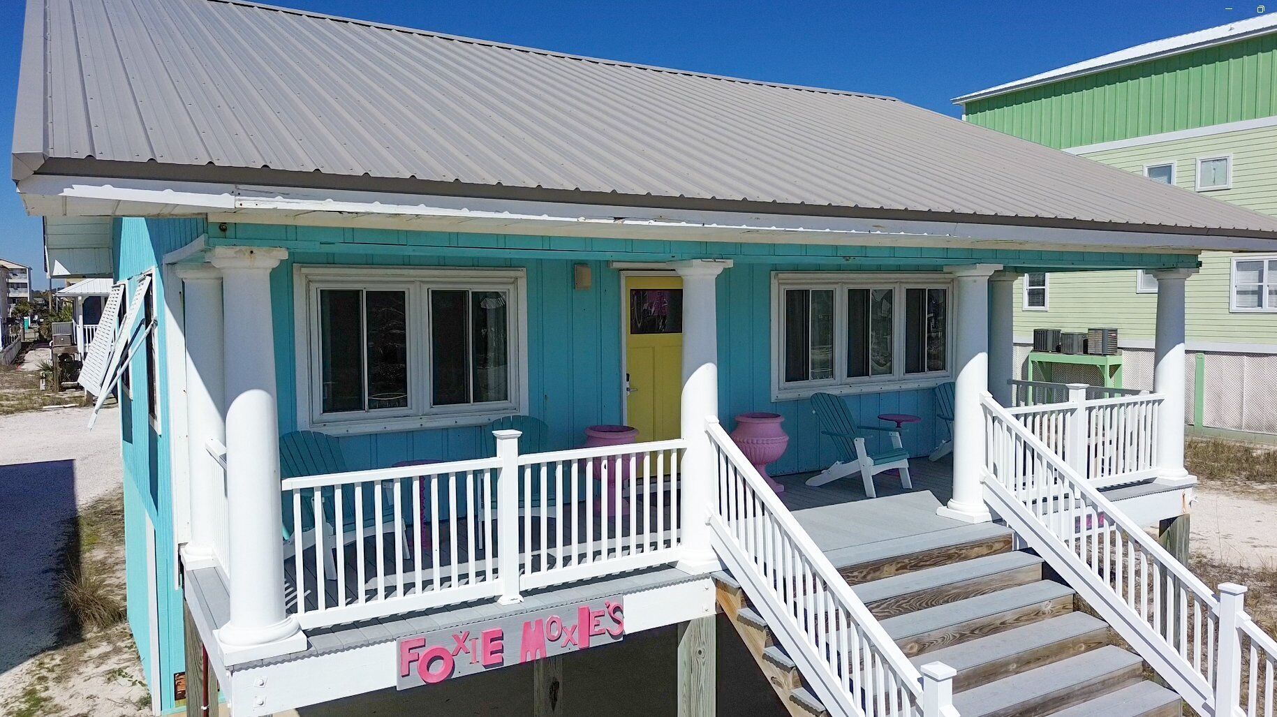 A beach house with a porch, a staircase, and a sign that reads "Foxie's".