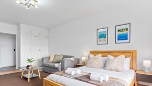 A neatly arranged bedroom with a bed, bedside tables, a sofa, and a wardrobe. - E1 Ventnor House - Studio Apartment, Sleeps 2 (Cape Town)