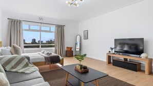 A modern hotel room with a bed, sofa, TV, and a view of the city. - E1 Ventnor House - Studio Apartment, Sleeps 2 (Cape Town)