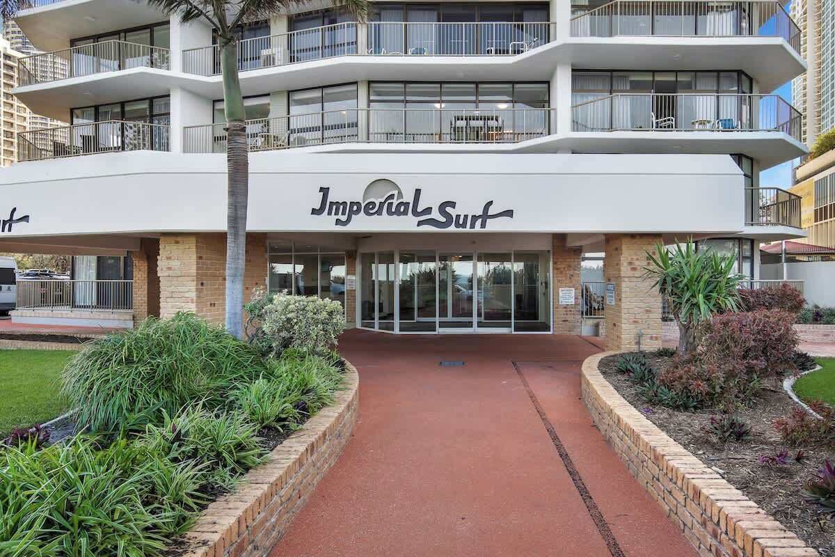 Ein mehrstöckiges Hotel namens „Imperial Surf“ mit modernem Design, inklusive Balkonen und einem begrünten Eingangsbereich.