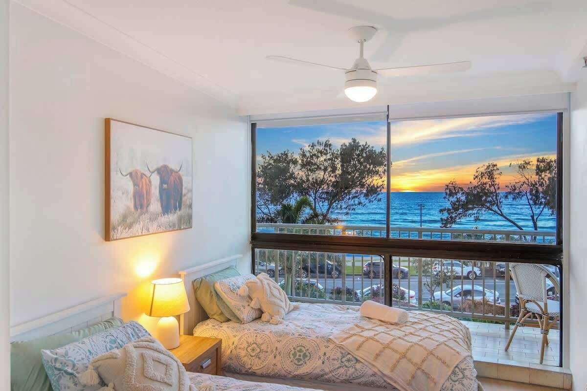 Ein Schlafzimmer mit großem Fenster mit Meerblick, einem Deckenventilator und einer Nachttischlampe.