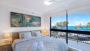 Una camera da letto con un letto grande, due lampade ai lati del letto, vista mare e un balcone con sedie in vimini.