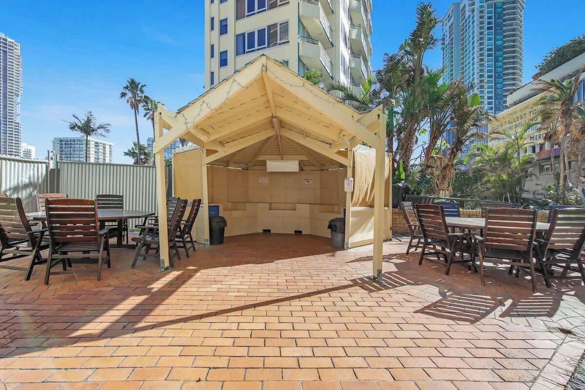 An outdoor patio area with a wooden pergola, brick flooring, and wooden tables and chairs.
