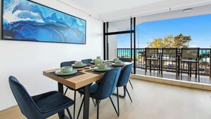 Un'area pranzo con un tavolo di legno apparecchiato per quattro persone, sedie blu e un grande quadro astratto appeso alla parete.