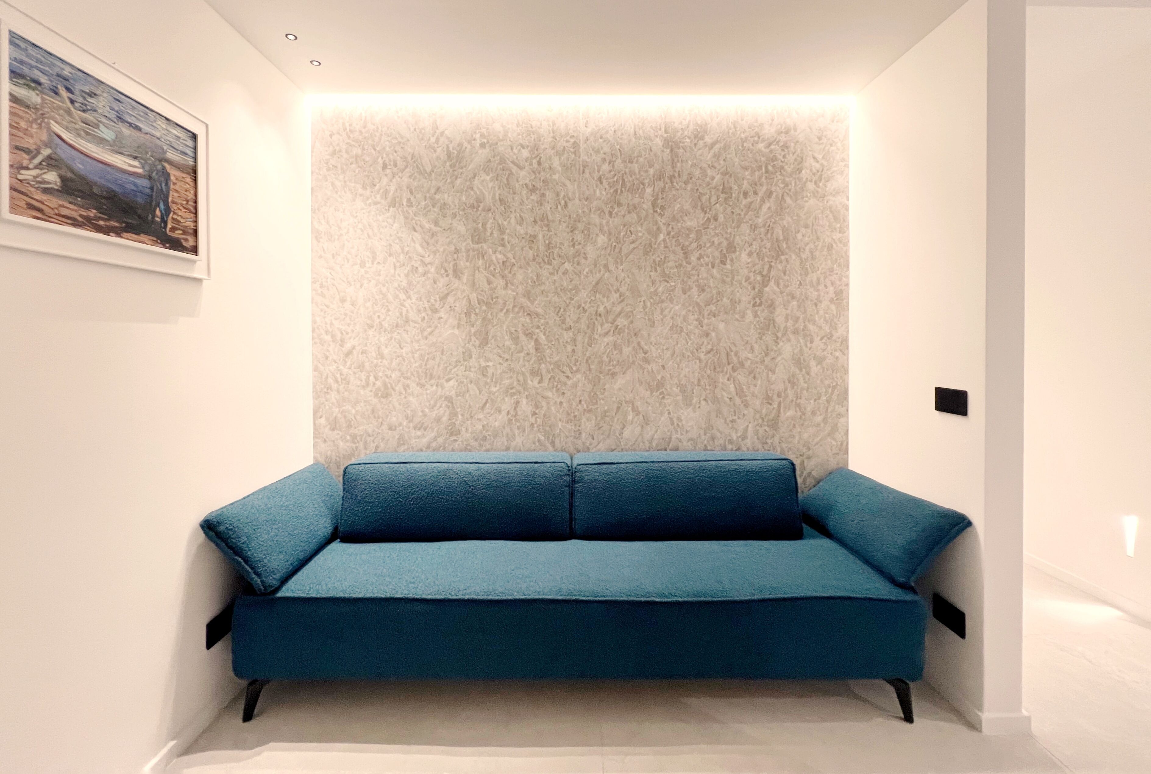 Quarto moderno com um sofá azul, parede texturizada e uma pintura emoldurada.