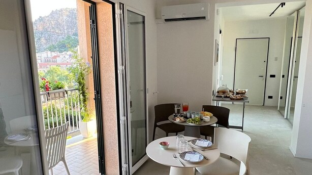 Een moderne eethoek met een tafel gedekt voor twee personen, een keuken op de achtergrond en een balkon met uitzicht op de stad.