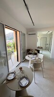 Un moderno comedor con una mesa dispuesta para dos, una cocina al fondo y un balcón con vistas a la ciudad.