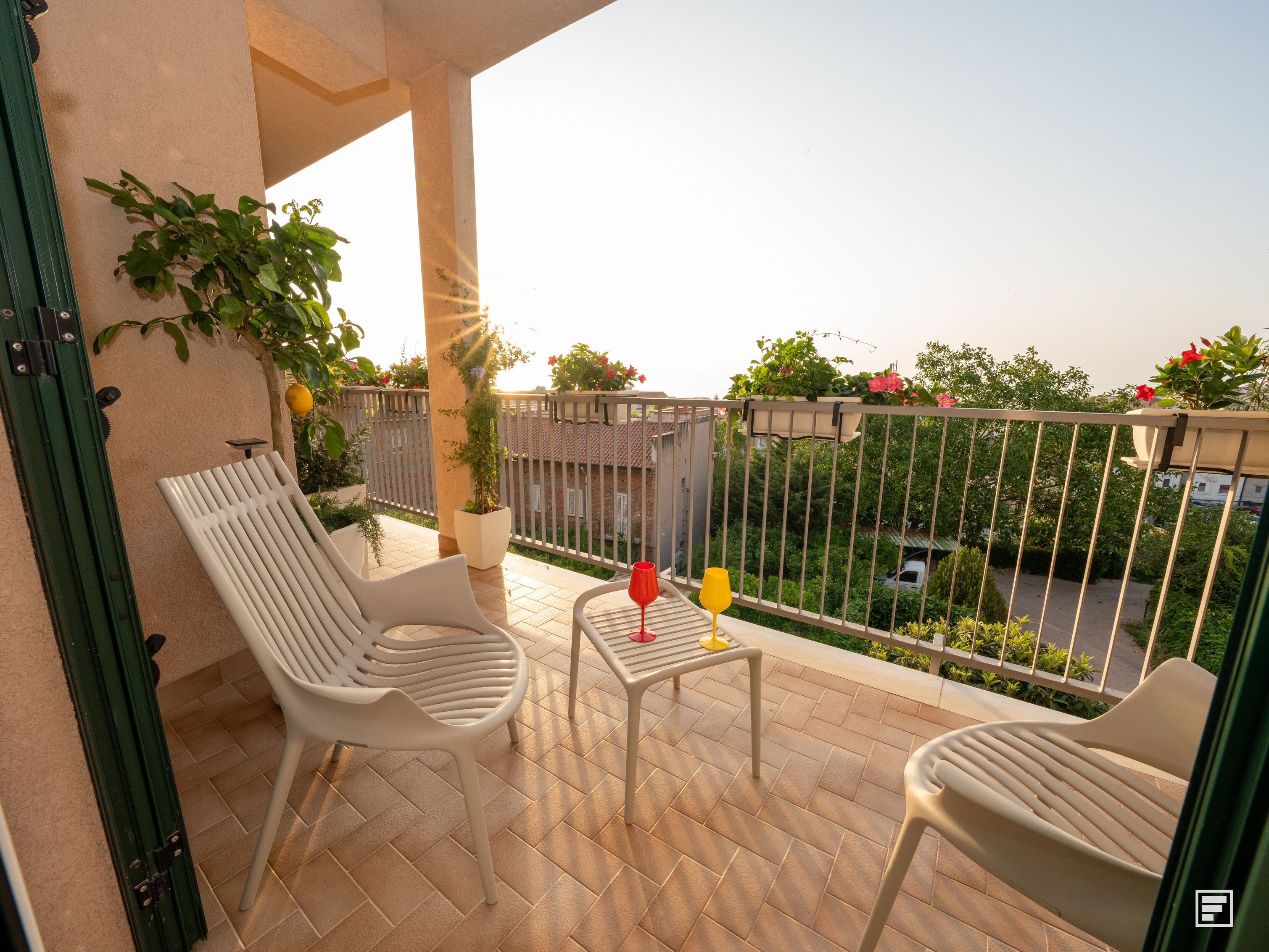 Een balkon met twee witte stoelen, een klein tafeltje en een bloempot.