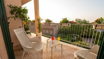 Een balkon met twee witte stoelen, een klein tafeltje en een bloempot.