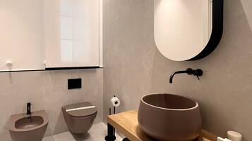 Un baño moderno con un lavabo redondo, un bidé y un espejo grande.