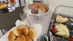 Een buffet met diverse gerechten, waaronder broodjes, een schaal fruit en een dessertpresentatie.
