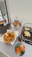 Una mesa de buffet con diversos alimentos, incluyendo panecillos, una cesta de fruta y una exposición de postres.