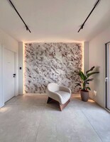 Un interior moderno con una pared con estampado de mármol, una butaca curvada y una planta en maceta.